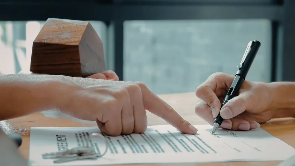One hand pointing to a signature line, and another hand signing the lease