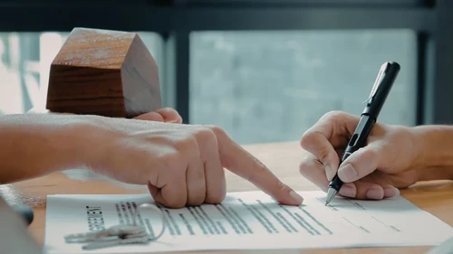 One hand pointing to a signature line, and another hand signing the lease