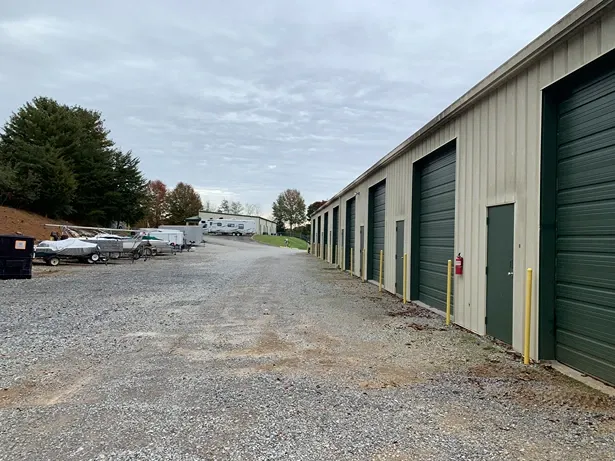 Wide-angle view of storage unit buildings and open gravel lot at Volunteer Storage Tellico Village with vehicle storage...